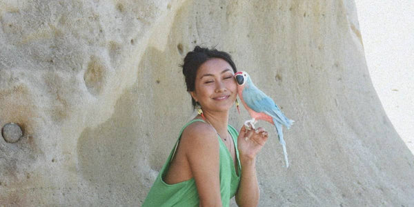 Woman wearing green jumpsuit holding a parrot at the beach
